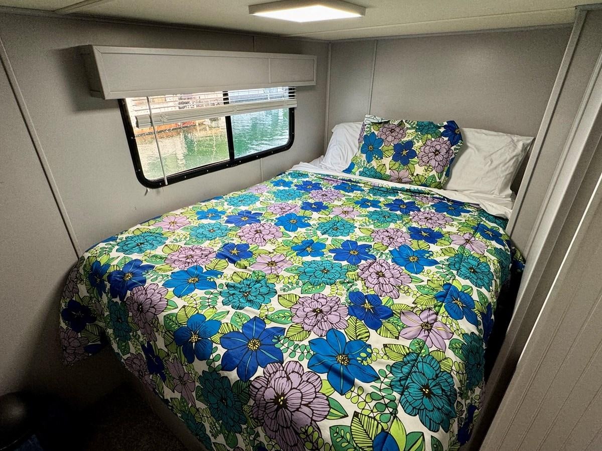 a bed with a flowered comforter and a window aboard 2012 MAJESTIC 16 X 75WB HOUSEBOAT NLSD Yacht for Sale