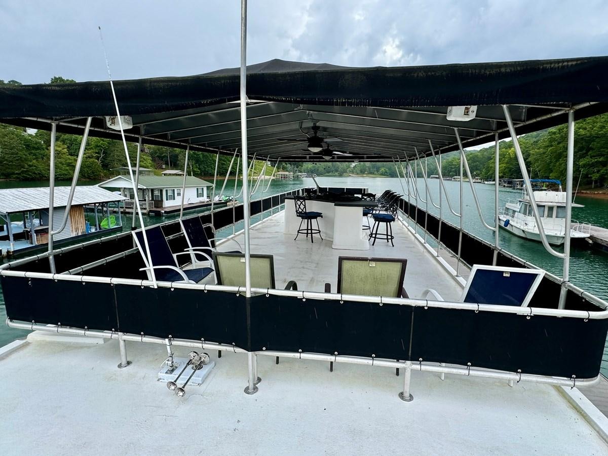 a deck with a chair and a table on it aboard 2012 MAJESTIC 16 X 75WB HOUSEBOAT NLSD Yacht for Sale