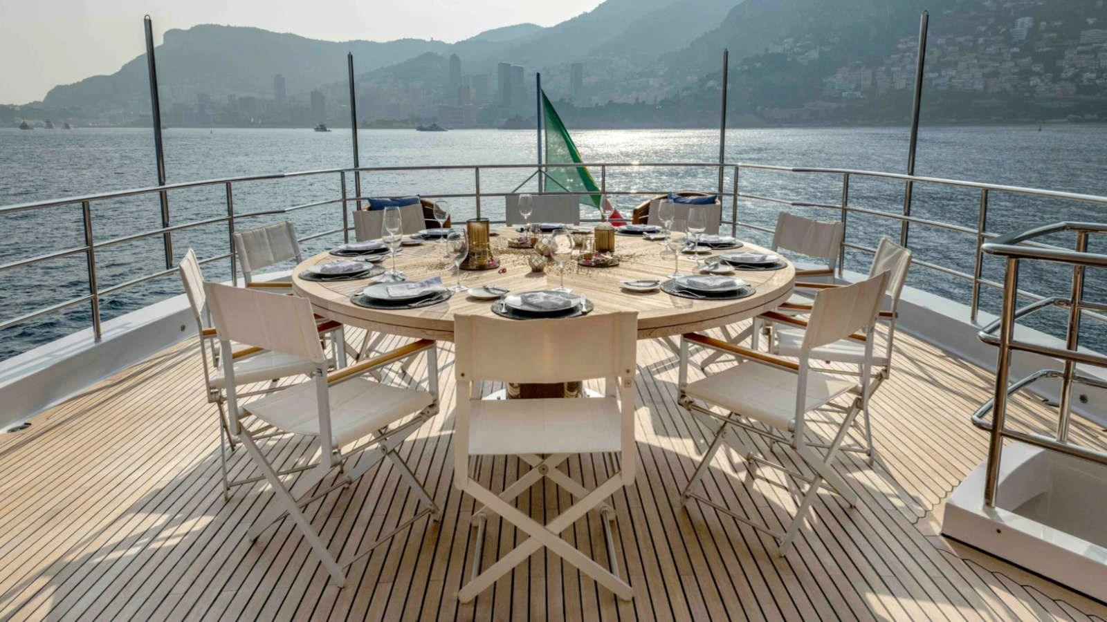 The aft deck features an elegant dining area with a round table set for a meal, offering stunning views of the surrounding waters and coastline. aboard PALMER JOHNSON 150 Yacht for Sale