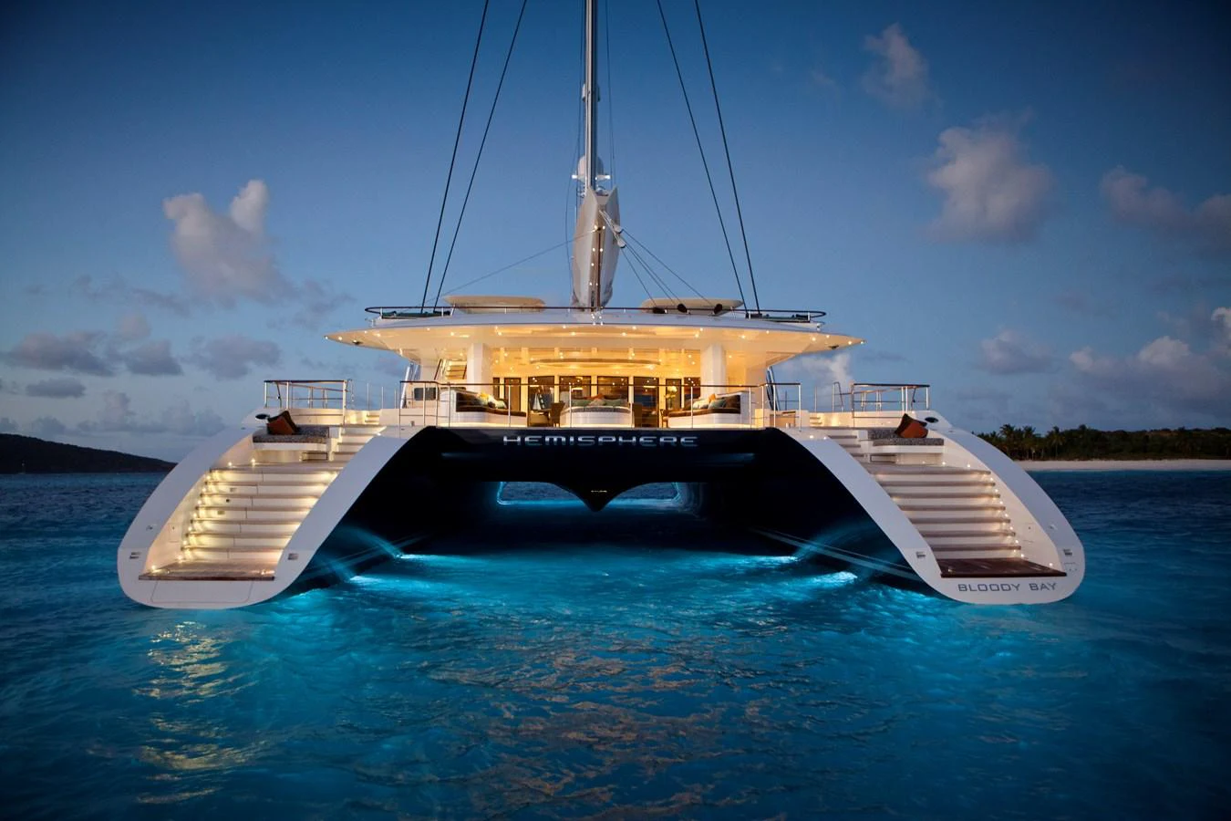 The yacht is beautifully illuminated at dusk, showcasing its impressive twin hull design and inviting aft deck. aboard HEMISPHERE Yacht for Sale