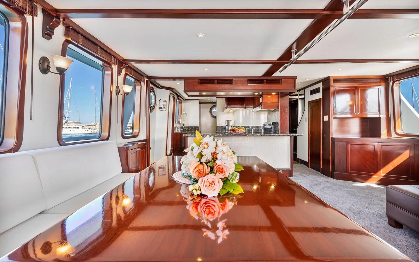 The yacht's dining area features a polished wooden table with a floral centerpiece, surrounded by large windows and elegant woodwork. aboard MISS SARAH J Yacht for Sale