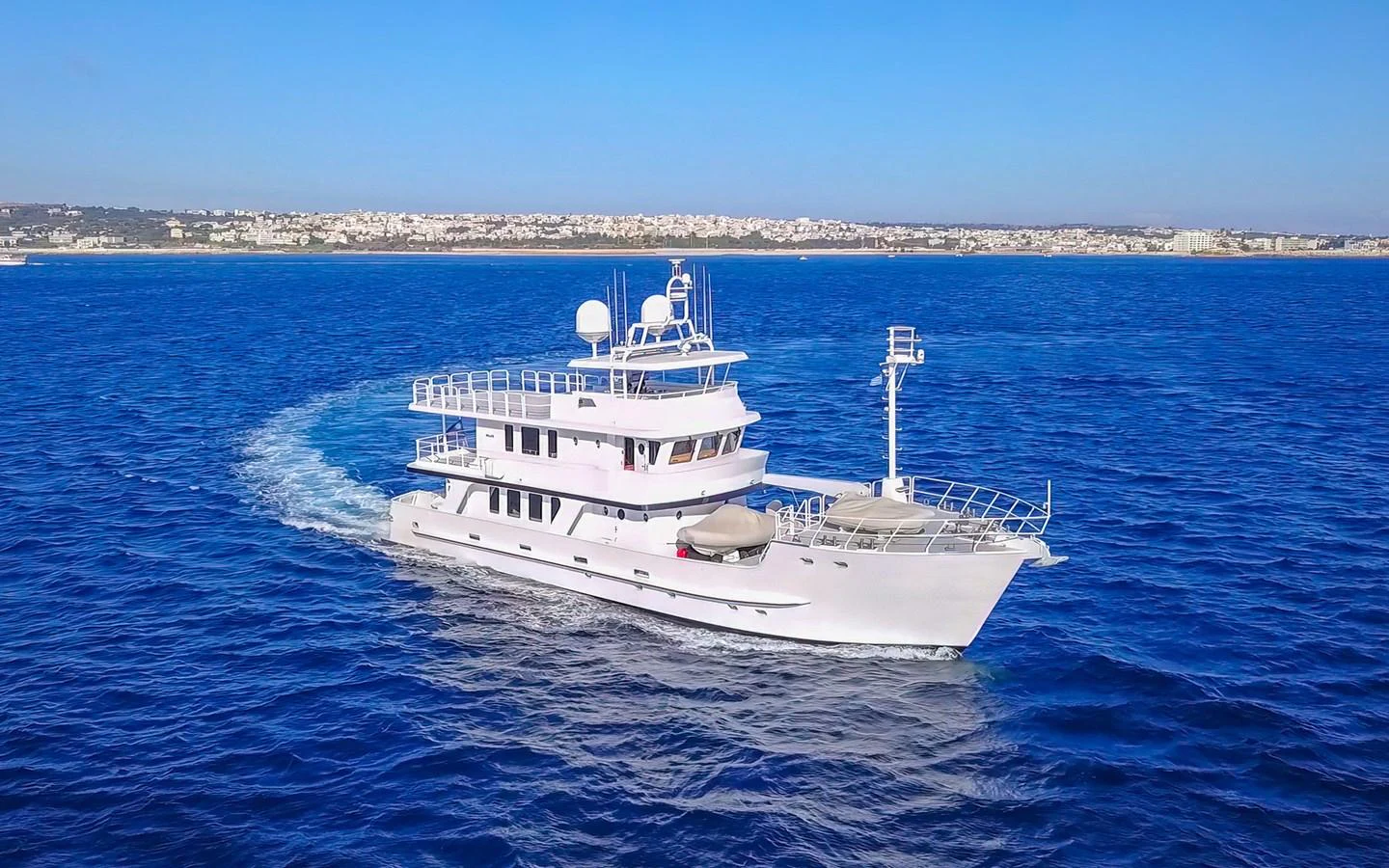 A sleek yacht cruises through the deep blue waters with a scenic coastline in the background. aboard MISS SARAH J Yacht for Sale