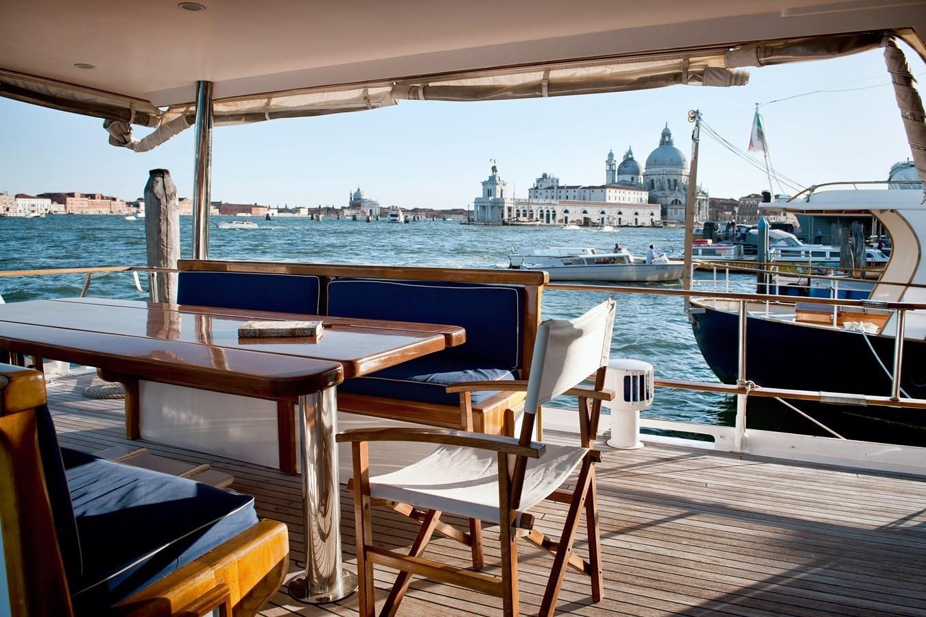 a table and chairs on a deck overlooking a body of water aboard LA BOUFFONNE Yacht for Sale