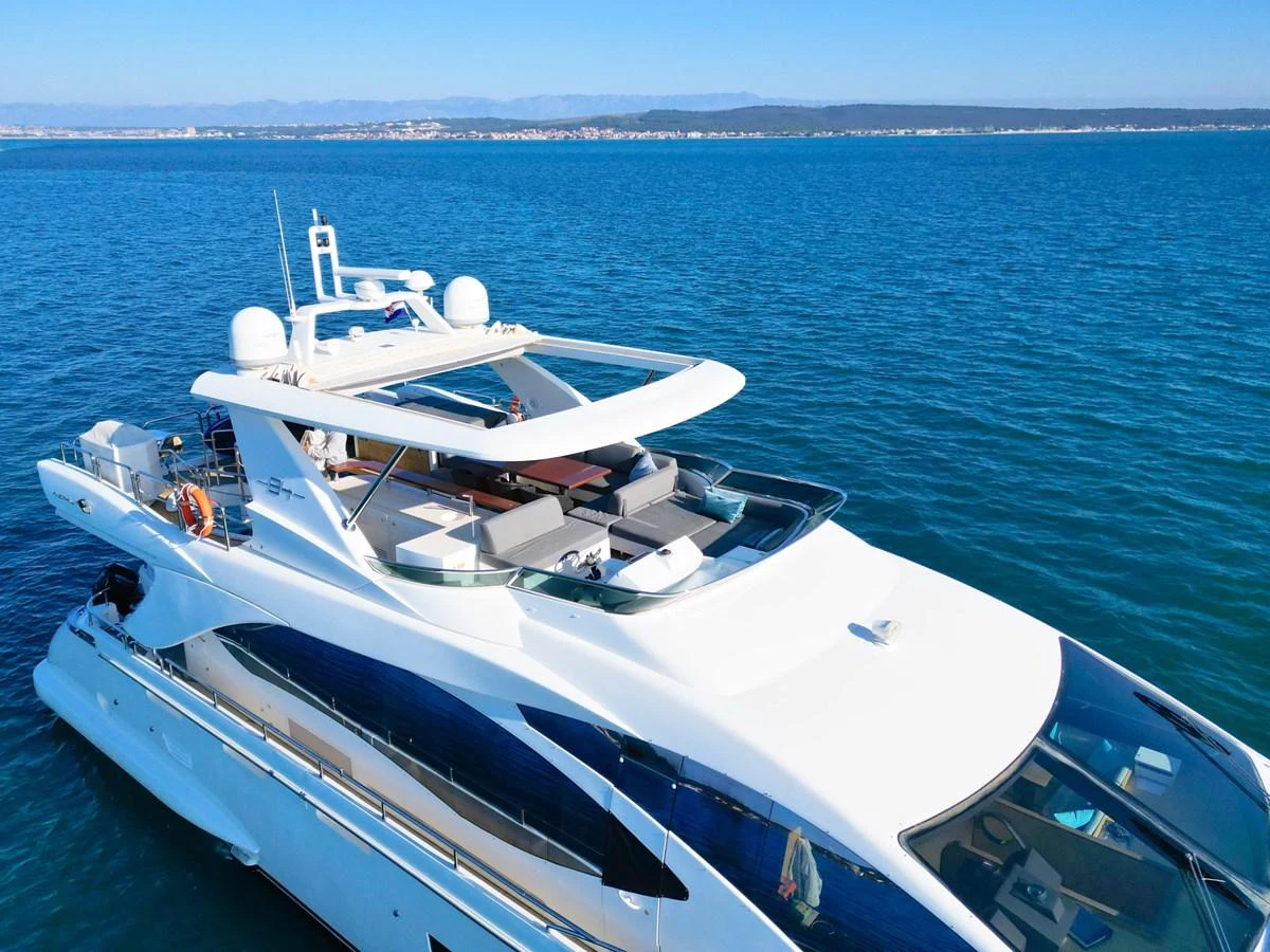 A sleek and modern yacht cruising on calm blue waters under a clear sky. aboard HUBO Yacht for Sale