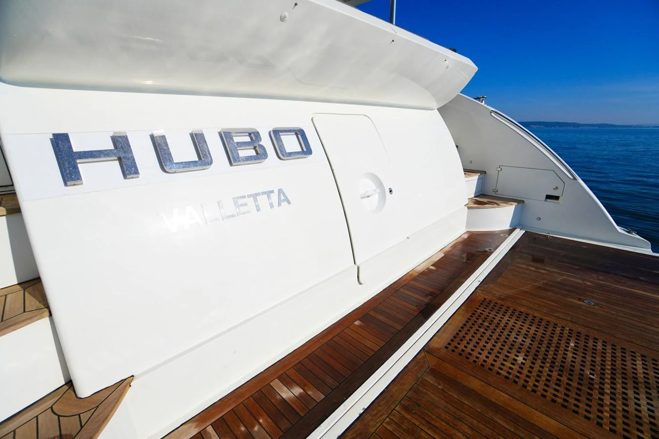 A close-up view of the yacht's stern showcasing the name and wooden deck. aboard HUBO Yacht for Sale