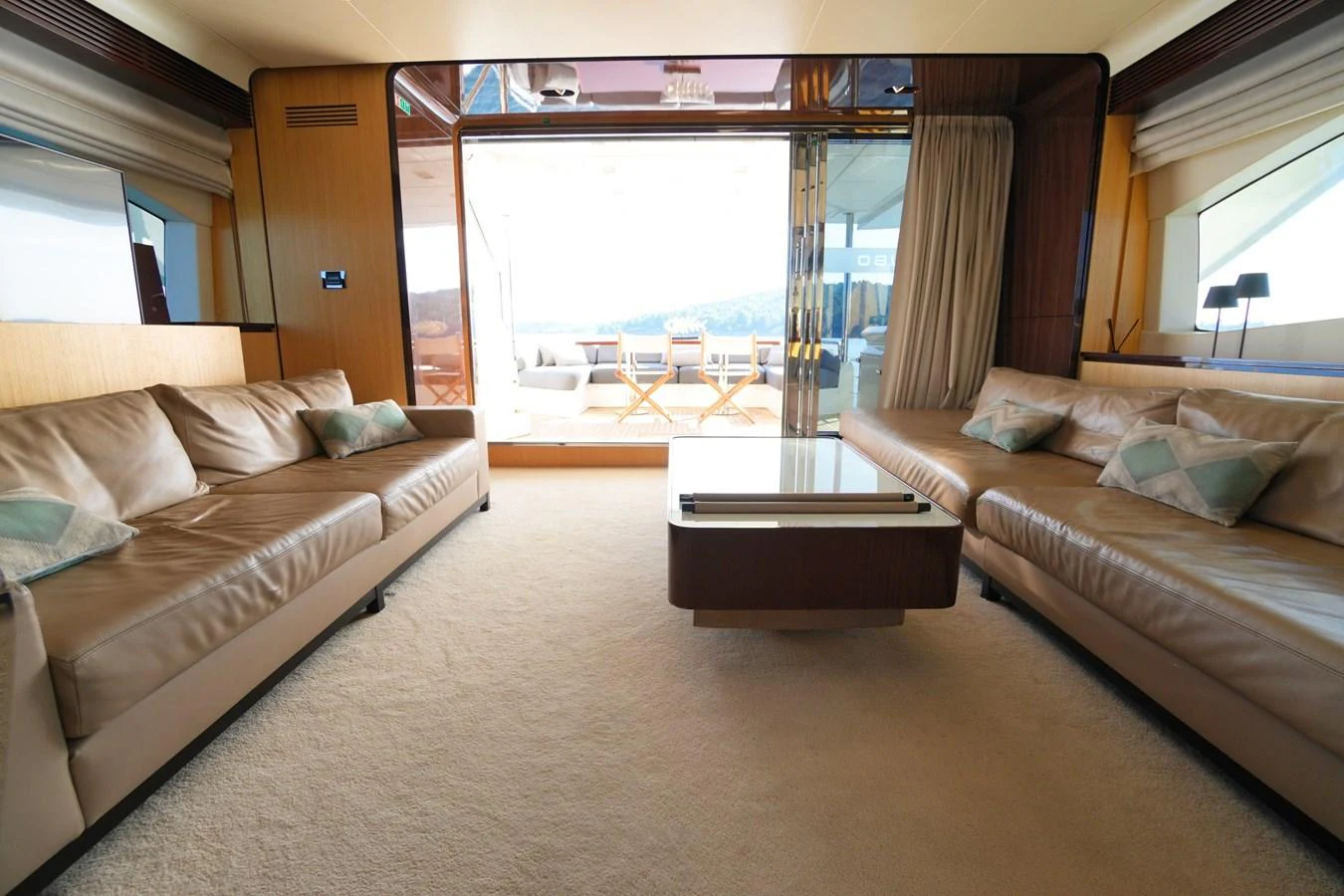 The salon features plush seating and a coffee table, opening up to an outdoor deck with a stunning view. aboard HUBO Yacht for Sale
