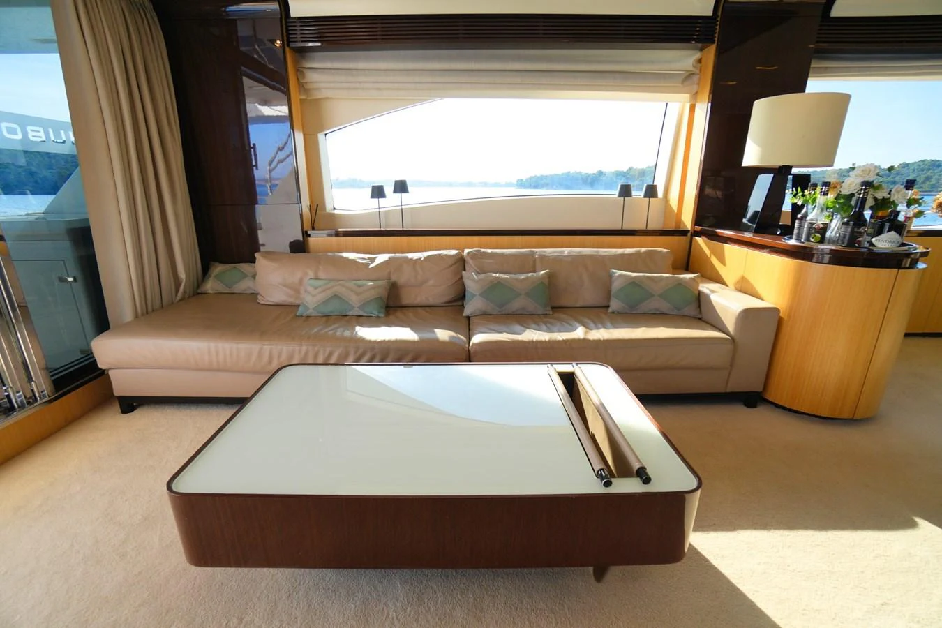The salon features a comfortable seating area with a large sofa and a stylish coffee table, bathed in natural light. aboard HUBO Yacht for Sale