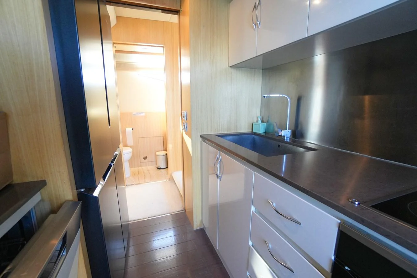 The yacht's galley features modern appliances and sleek cabinetry, leading to a well-lit bathroom area. aboard HUBO Yacht for Sale