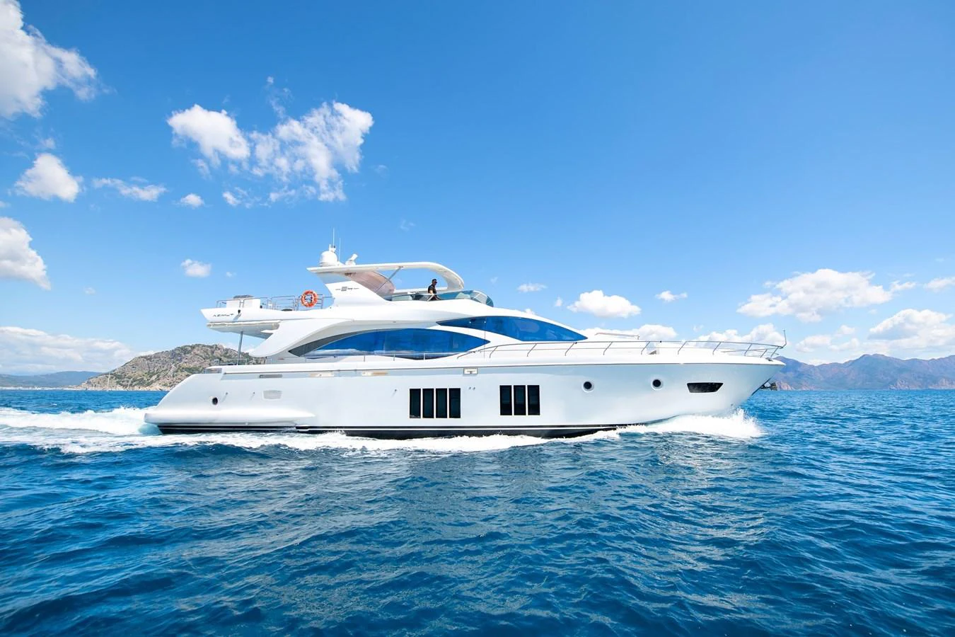 A sleek and modern yacht cruising on a clear blue sea under a bright sky. aboard HUBO Yacht for Sale