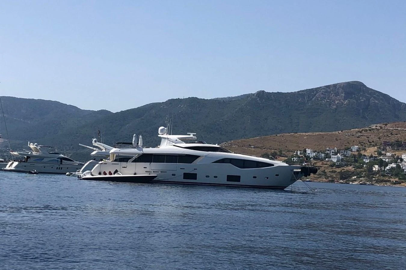 A sleek and modern yacht is anchored in a serene coastal area with scenic hills in the background. aboard HAPPY 2 Yacht for Sale