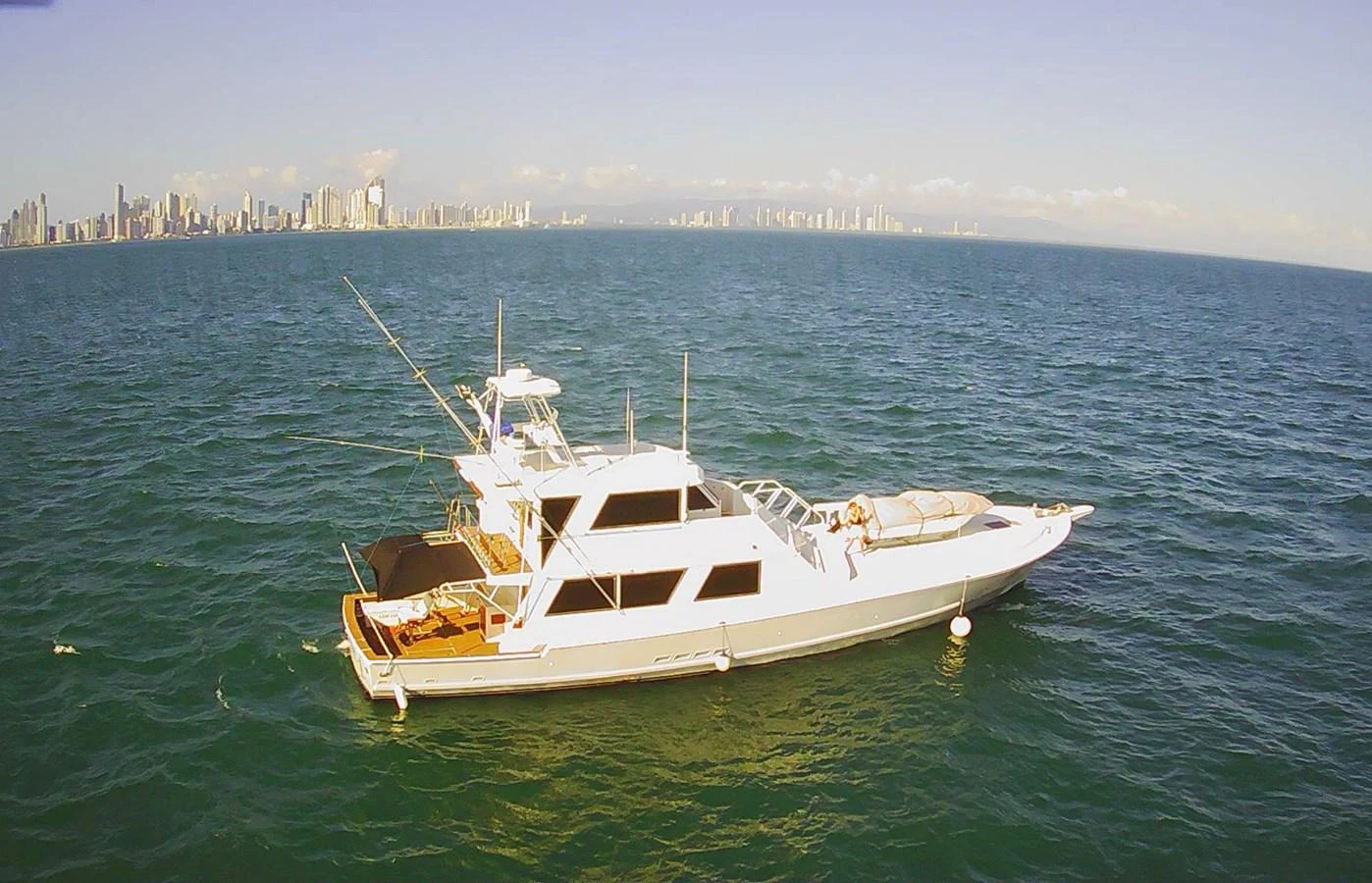 A sleek yacht cruises on calm waters with a city skyline in the background. aboard ADDISYN ANN Yacht for Sale