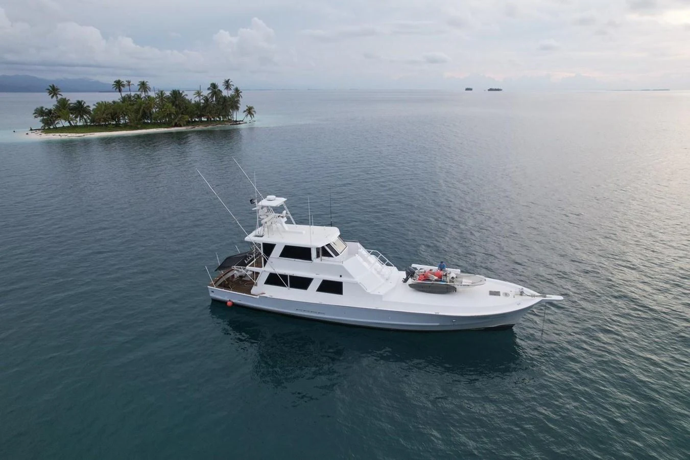 A sleek white yacht cruises near a small tropical island, showcasing its elegant design against a serene ocean backdrop. aboard ADDISYN ANN Yacht for Sale