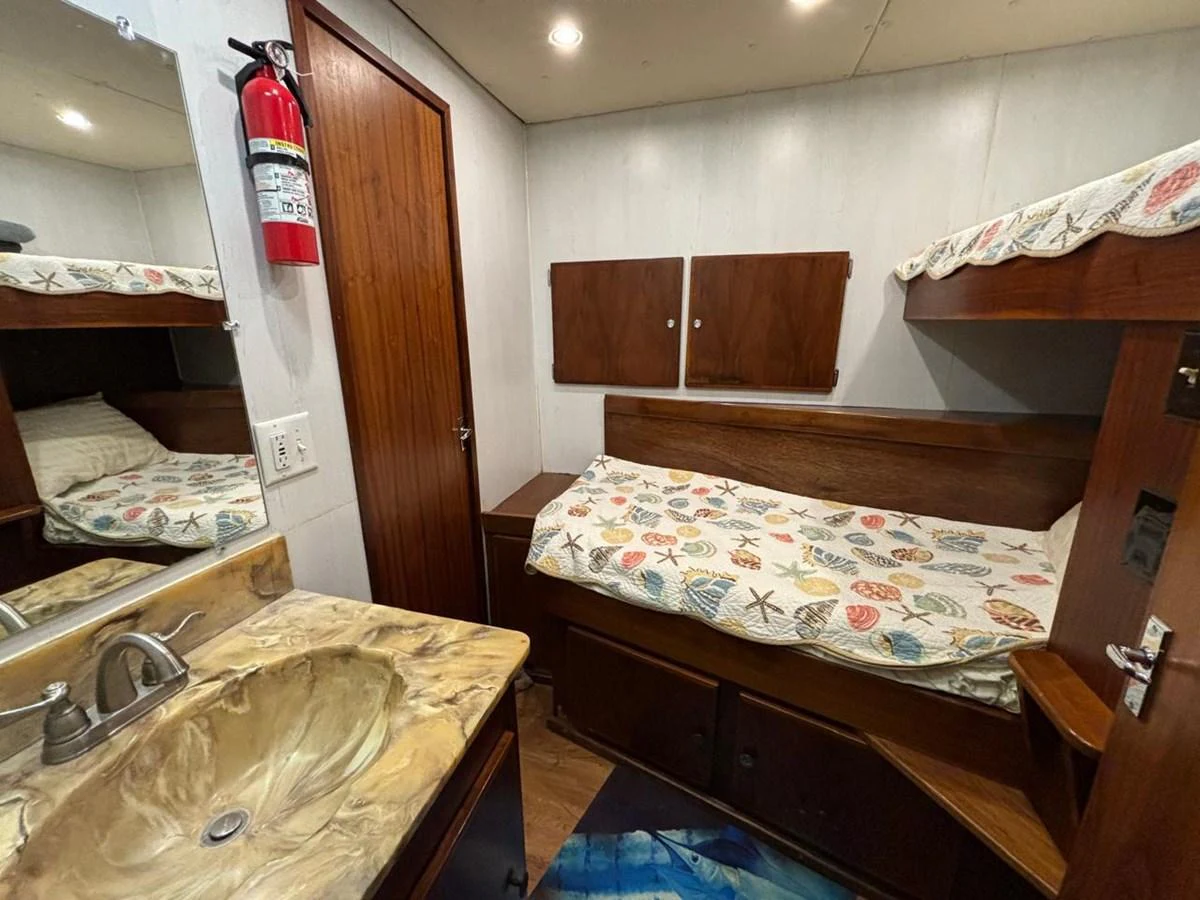 A cozy cabin with bunk beds and a small sink area, featuring warm wood finishes and nautical-themed bedding. aboard ADDISYN ANN Yacht for Sale