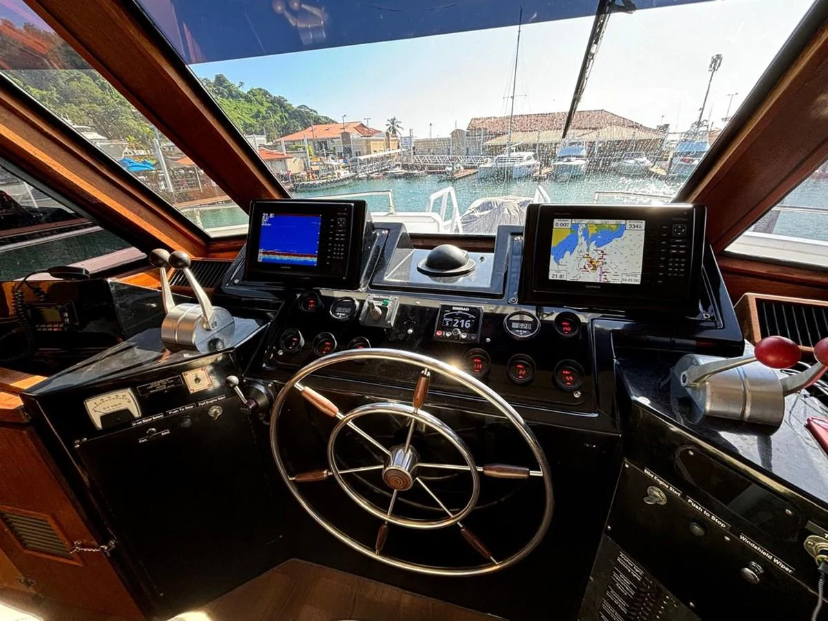 The helm station features advanced navigation equipment and a classic steering wheel, offering a commanding view of the marina. aboard ADDISYN ANN Yacht for Sale