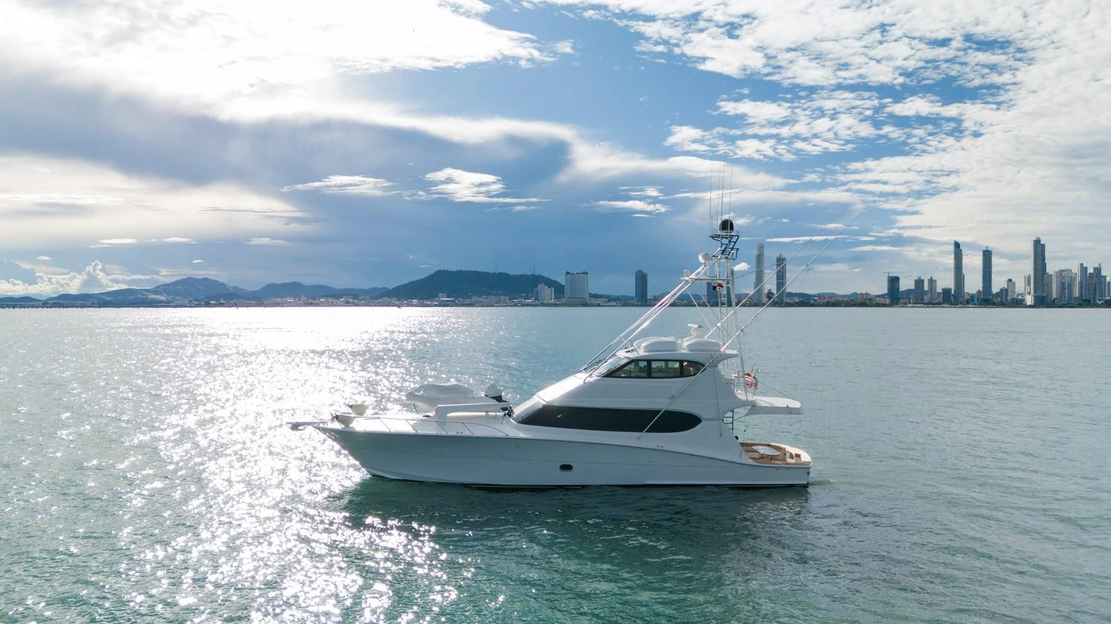 A sleek yacht cruises on calm waters with a cityscape in the background. aboard VIDA 1 Yacht for Sale