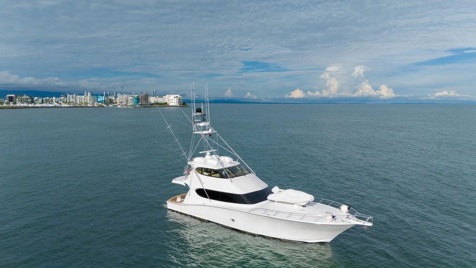 A sleek white yacht cruises gracefully on calm waters with a cityscape in the background. aboard VIDA 1 Yacht for Sale