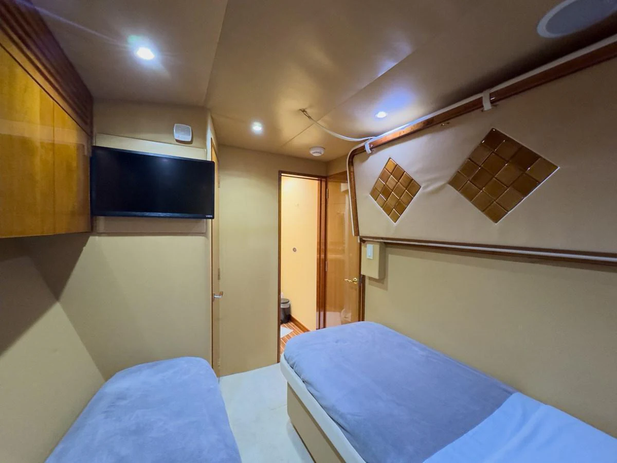 The guest cabin features twin beds, a wall-mounted TV, and warm wood accents. aboard VIDA 1 Yacht for Sale