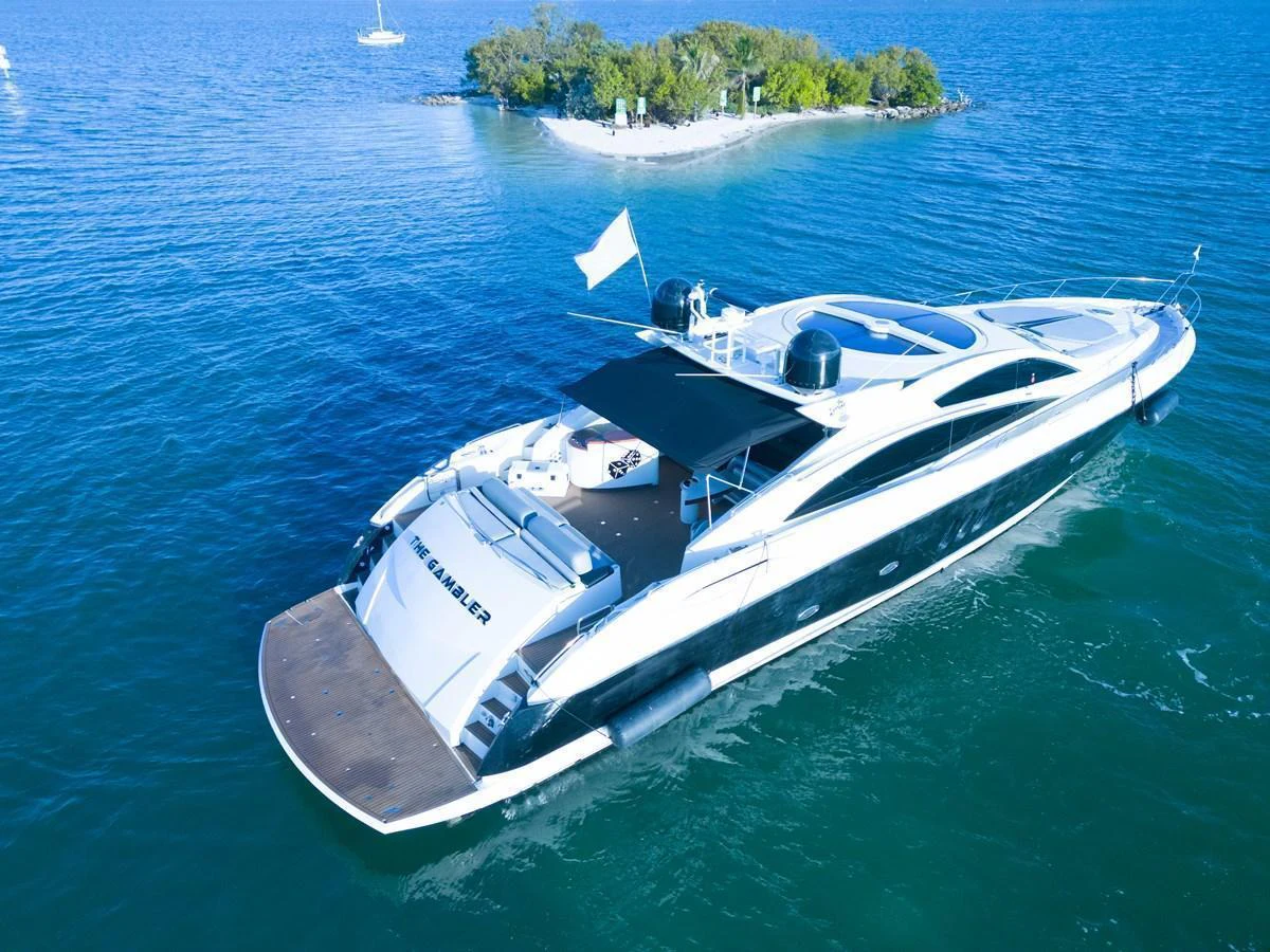 A sleek yacht cruises through clear blue waters near a small island. aboard THE GAMBLER Yacht for Sale