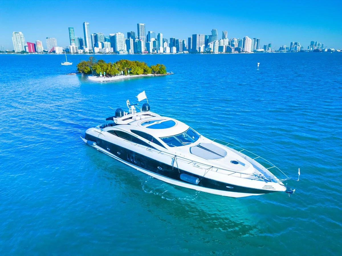 A sleek yacht cruises through vibrant blue waters with a city skyline in the background. aboard THE GAMBLER Yacht for Sale
