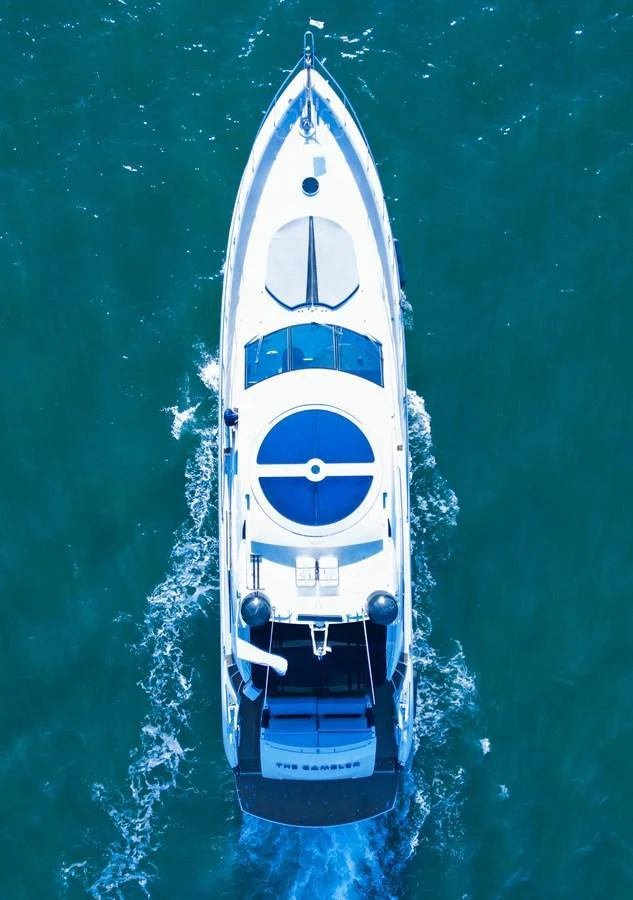 A sleek yacht cruises through clear blue waters, viewed from above. aboard THE GAMBLER Yacht for Sale