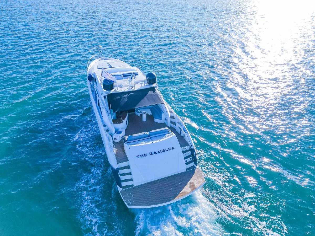 A sleek yacht cruises through clear blue waters, showcasing its spacious aft deck and elegant design. aboard THE GAMBLER Yacht for Sale