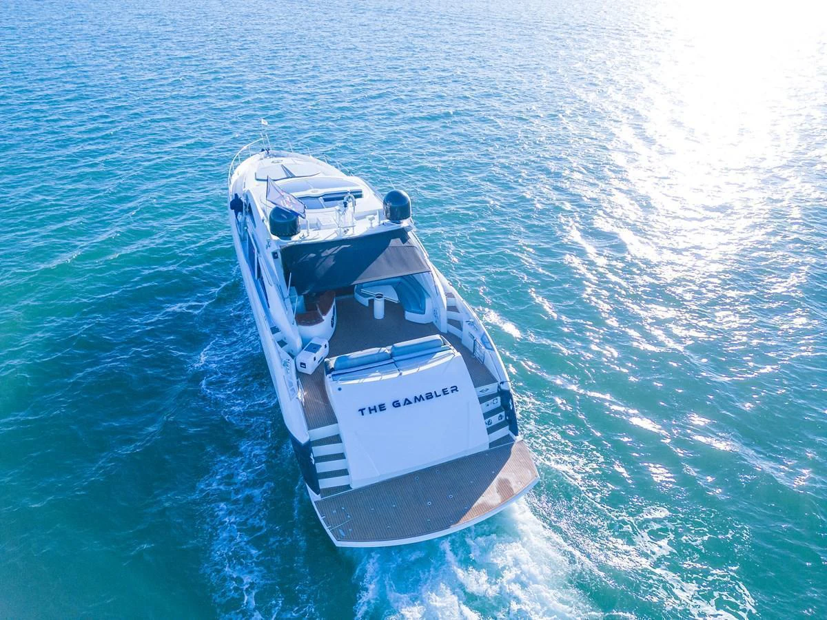 A sleek yacht glides through clear blue waters, showcasing its elegant design and spacious deck. aboard THE GAMBLER Yacht for Sale