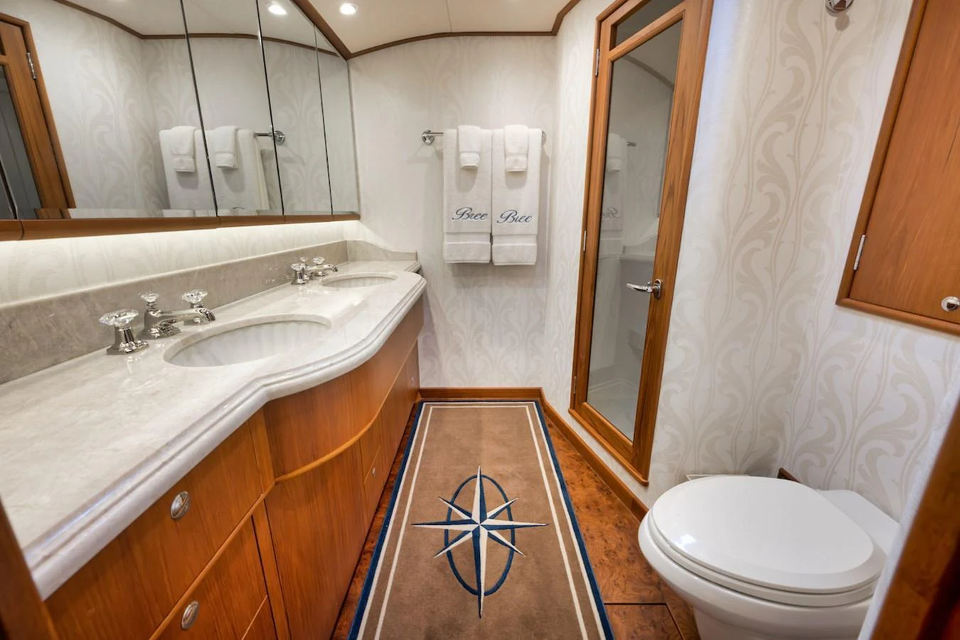 The yacht's bathroom features elegant wood cabinetry, a marble countertop, and a plush rug with a nautical design. aboard BREE Yacht for Sale