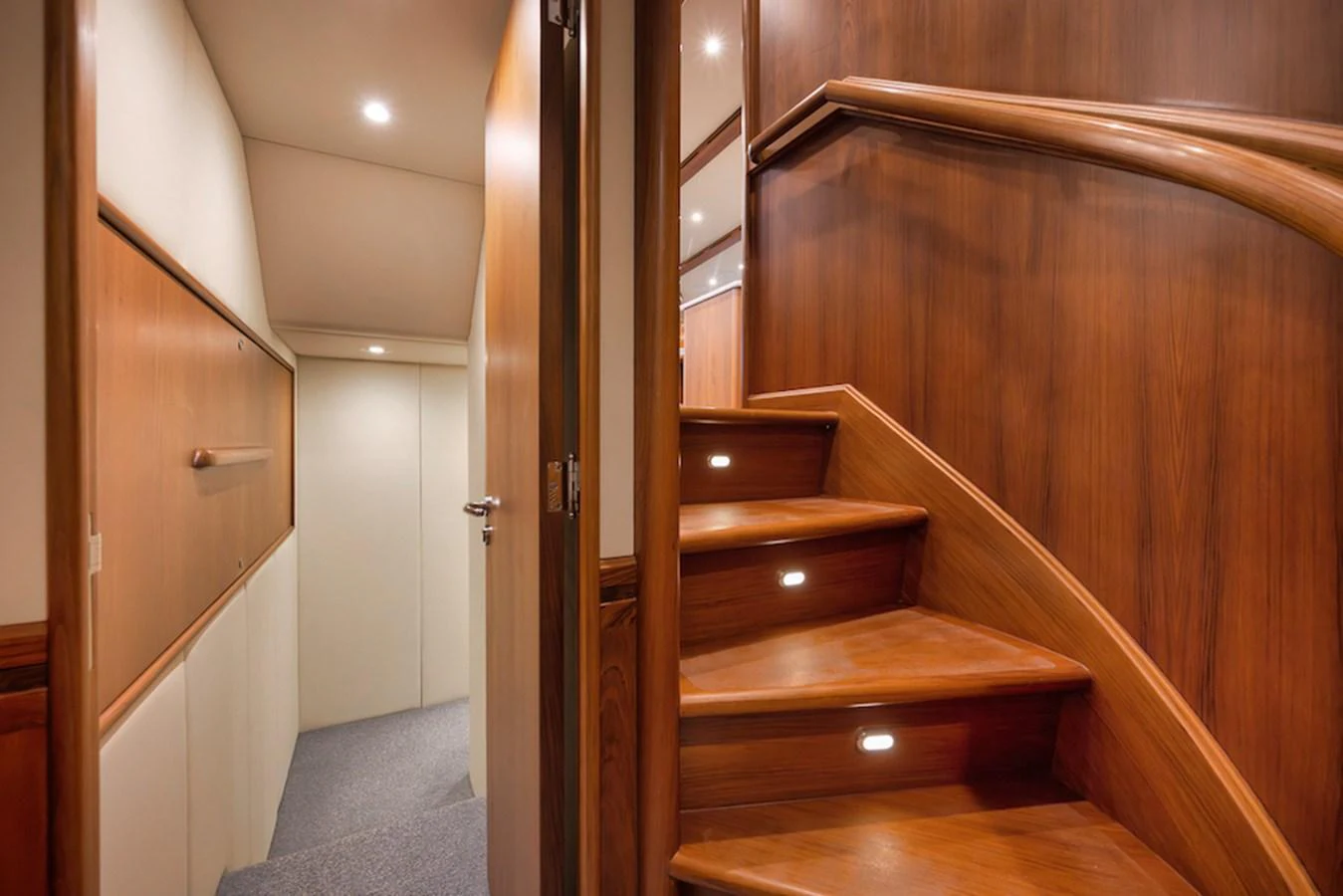 A beautifully crafted wooden staircase leads to the lower deck, showcasing elegant design and warm lighting. aboard BREE Yacht for Sale