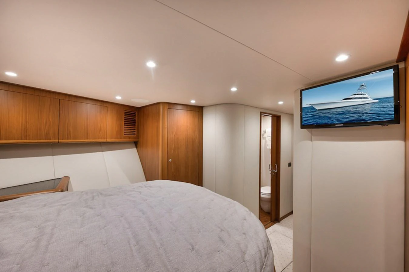The stateroom features a cozy bed, wooden cabinetry, and a mounted TV displaying a yacht image. aboard BREE Yacht for Sale