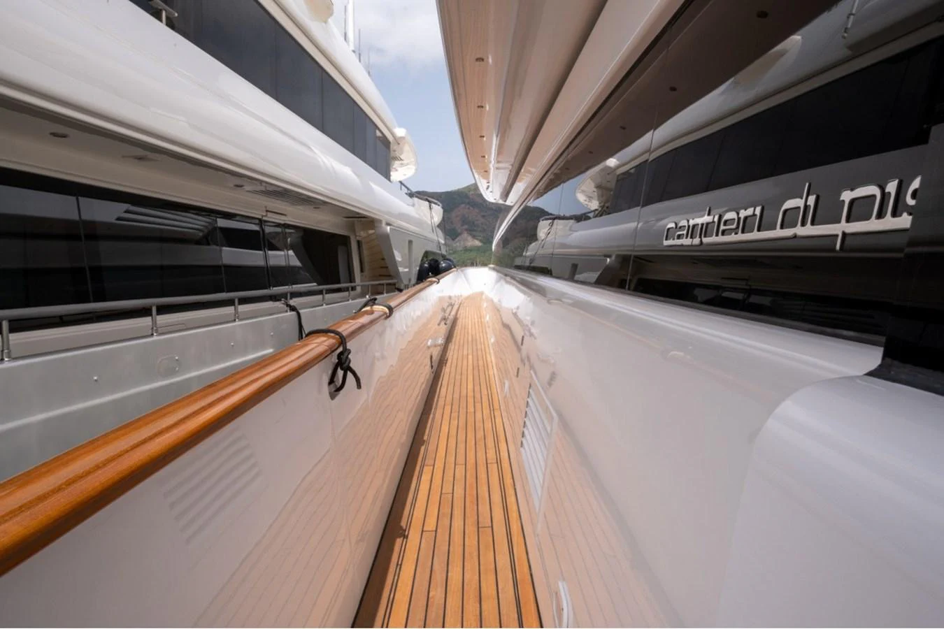 A sleek side deck with polished wood and white surfaces, flanked by two yachts in a marina. aboard PARSLEY Yacht for Sale
