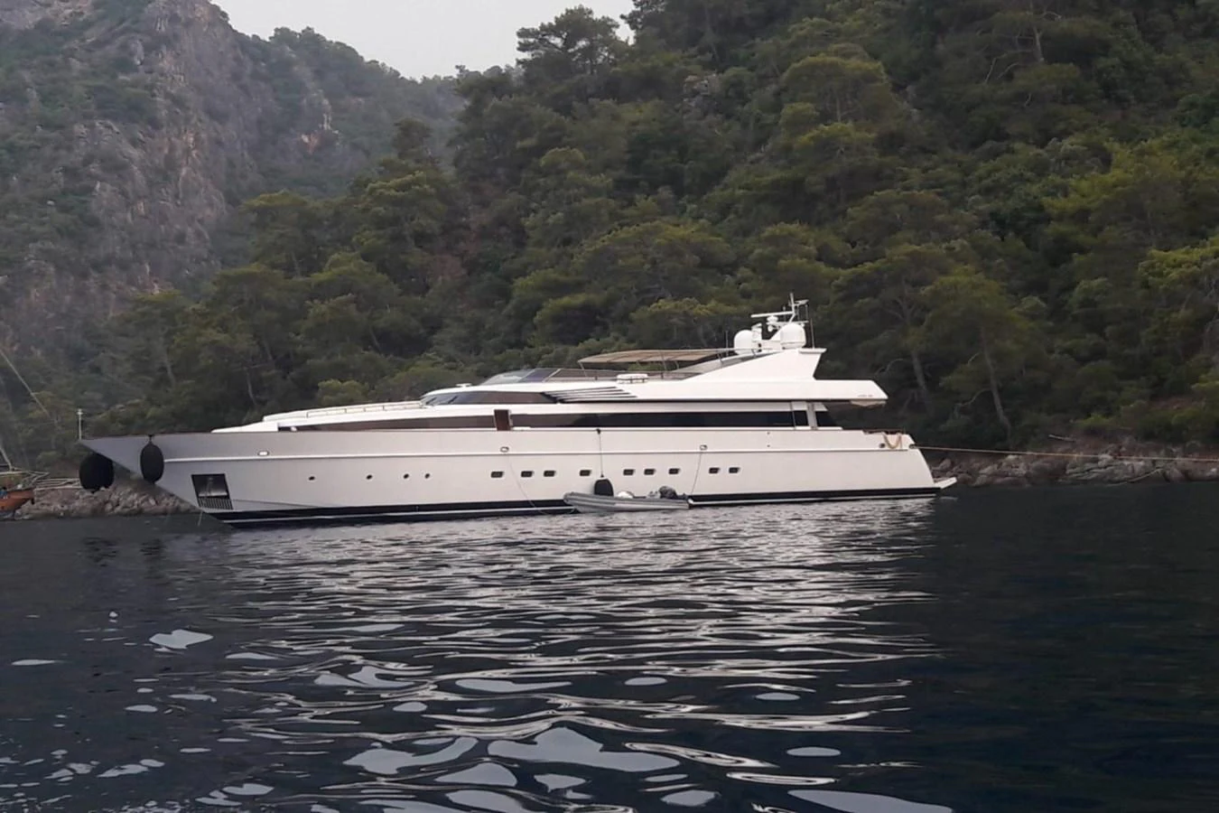 A sleek white yacht is anchored near a lush, forested coastline. aboard PARSLEY Yacht for Sale