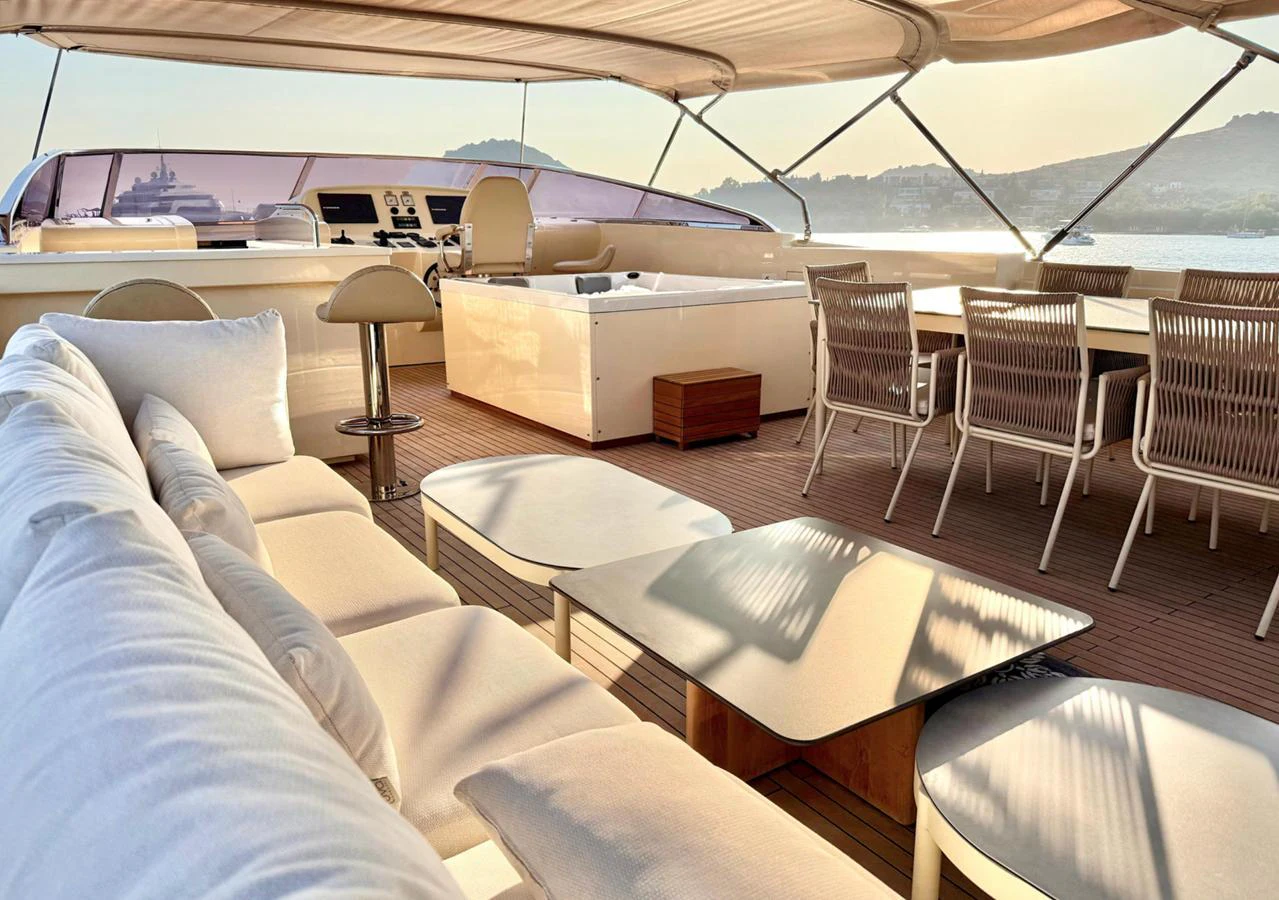 The flybridge offers a luxurious seating area with a dining table and helm station, all under a shaded canopy. aboard RIVA 115 Yacht for Sale