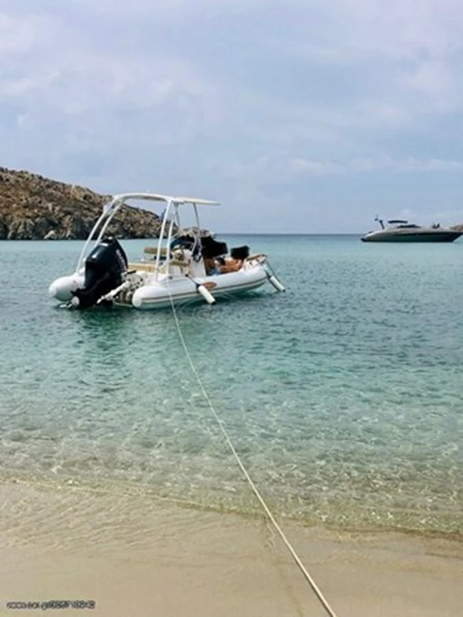 A tender is anchored in shallow, clear waters near a sandy beach with a yacht in the background. aboard PUMABAY Yacht for Sale