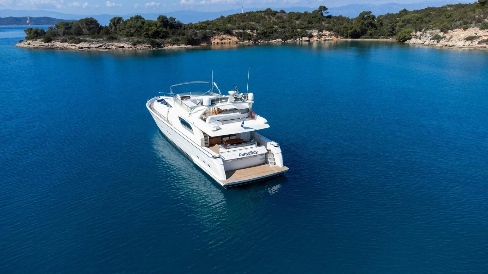 A sleek yacht cruises through serene blue waters near a picturesque coastline. aboard PUMABAY Yacht for Sale