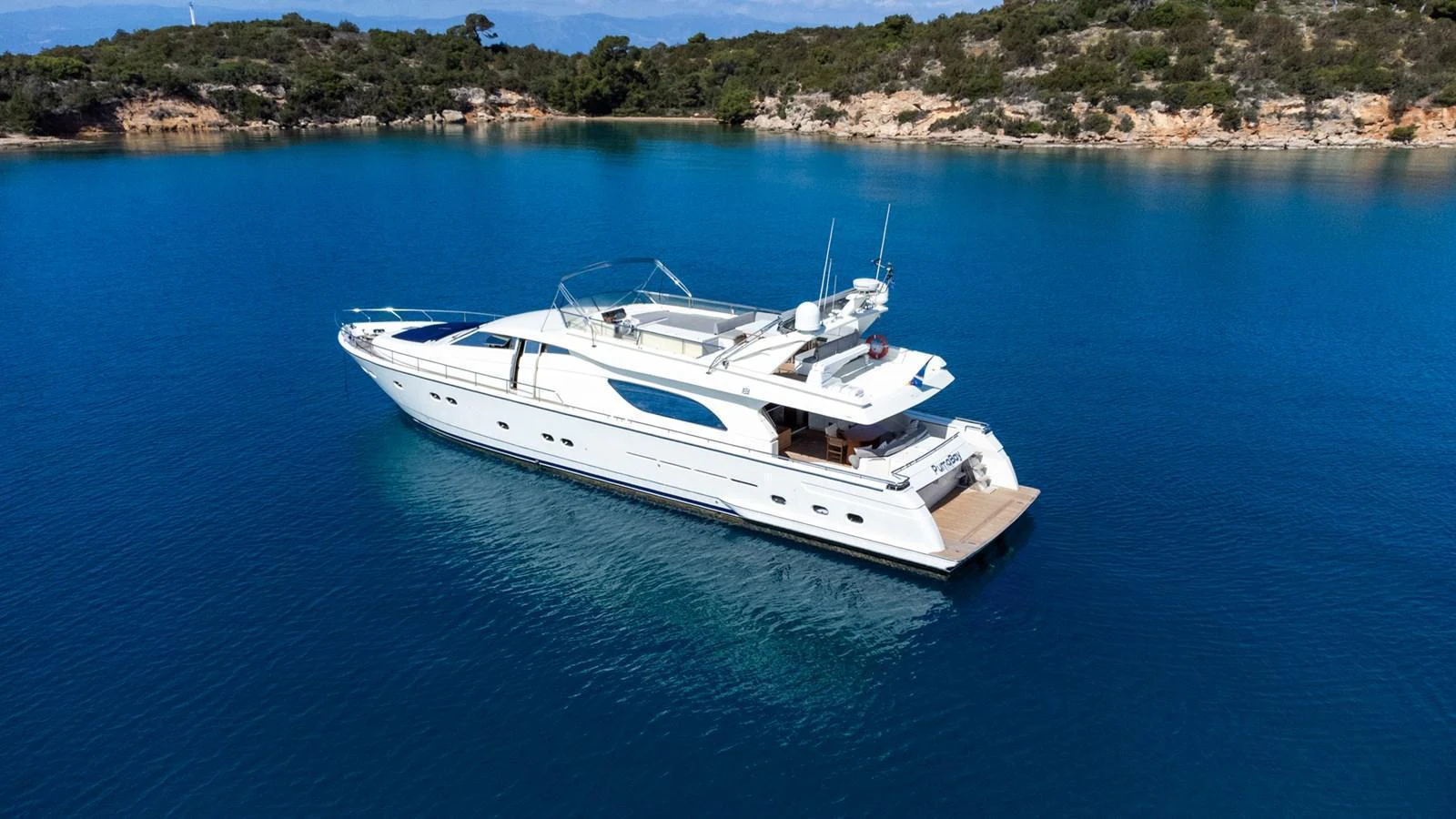 A sleek and modern yacht is anchored in a serene, turquoise bay with lush greenery in the background. aboard PUMABAY Yacht for Sale