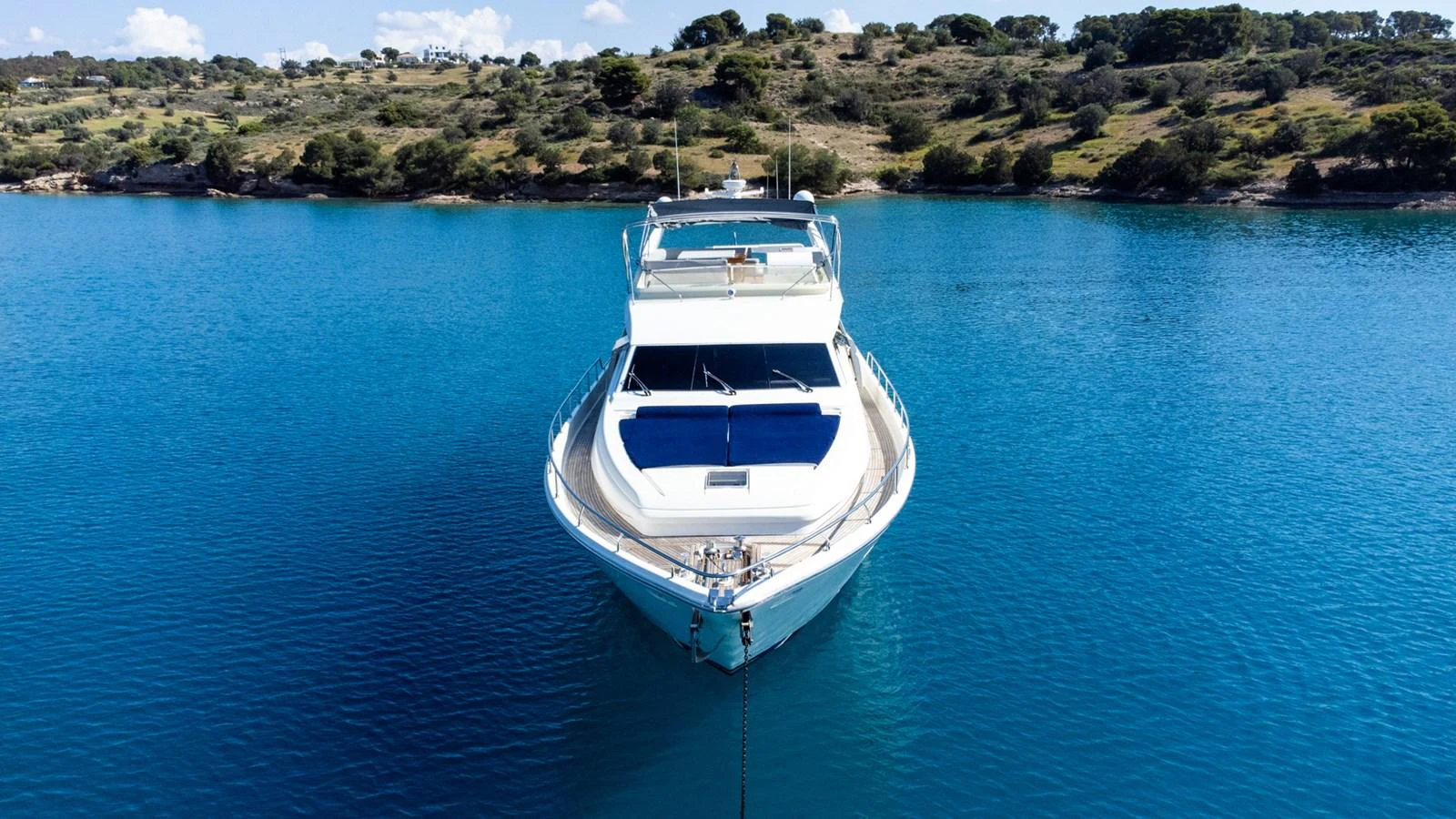 A sleek yacht is anchored in tranquil blue waters with a scenic backdrop. aboard PUMABAY Yacht for Sale