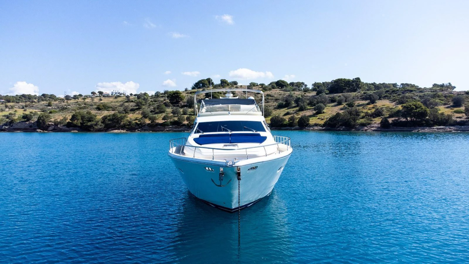 A sleek yacht is anchored in tranquil blue waters with a scenic shoreline in the background. aboard PUMABAY Yacht for Sale