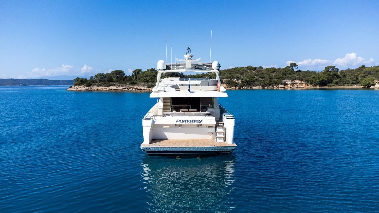 A luxurious yacht is anchored in a serene, clear blue bay with lush greenery in the background. aboard PUMABAY Yacht for Sale