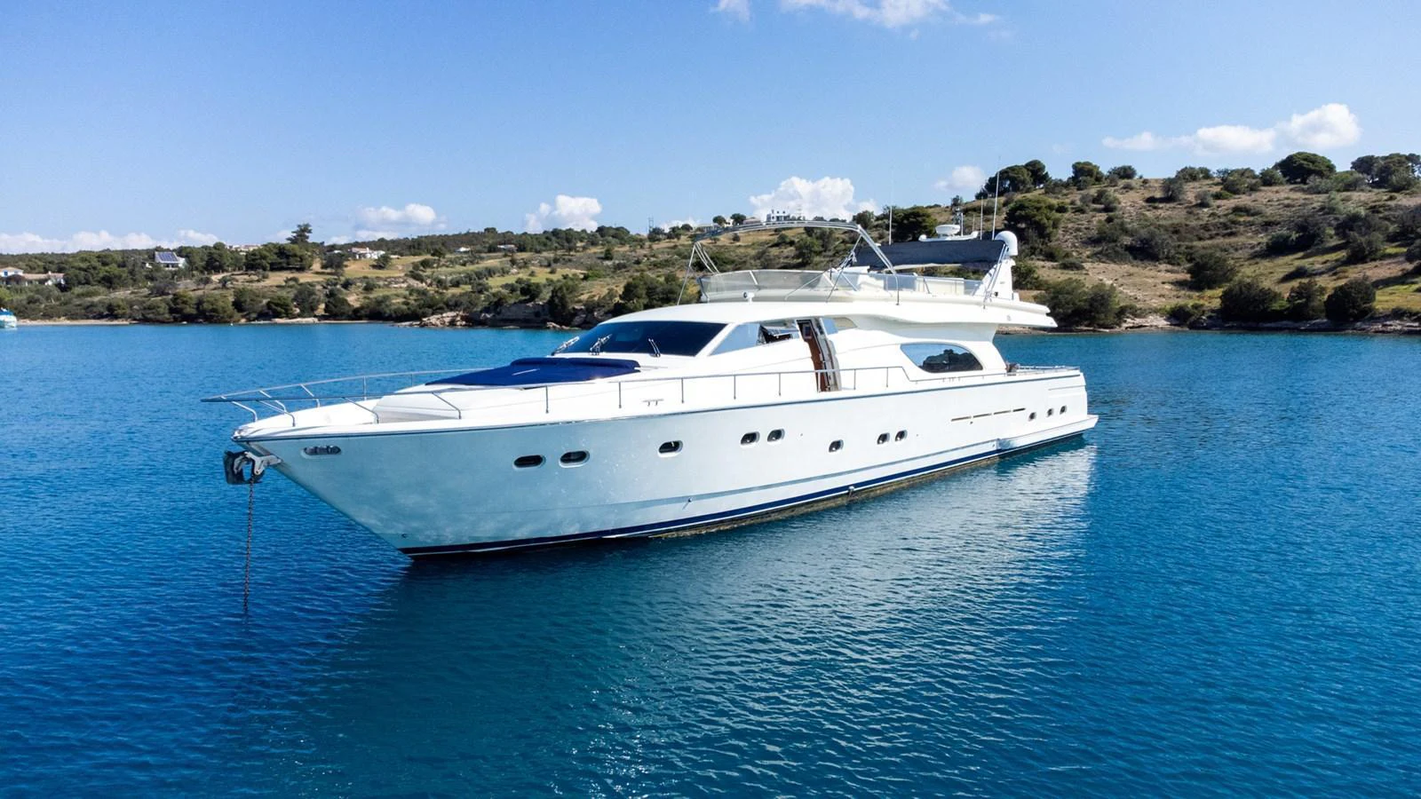A sleek, white yacht is anchored in calm, clear blue waters near a scenic coastline. aboard PUMABAY Yacht for Sale