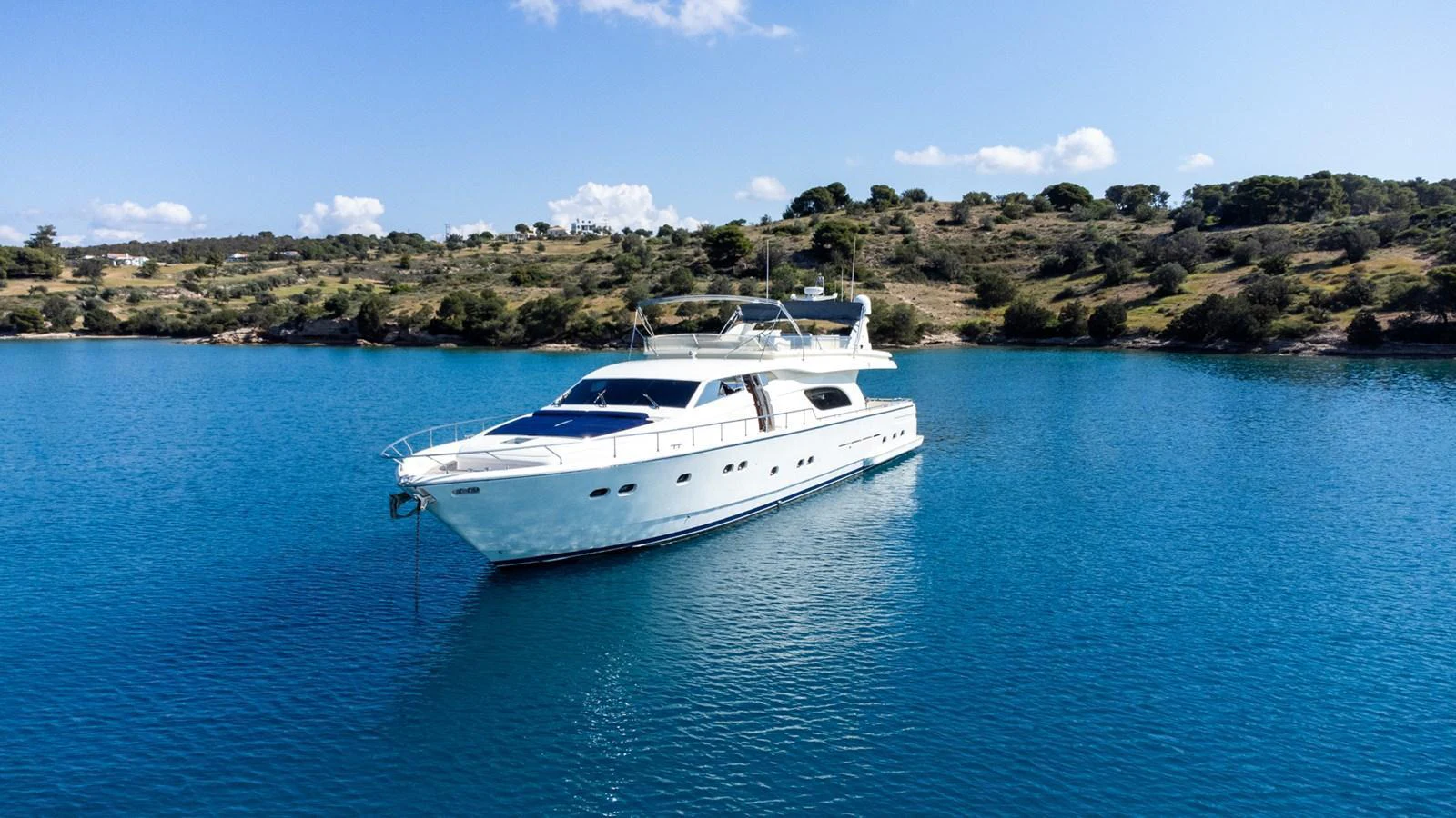 A sleek yacht is anchored in a serene, turquoise bay with a scenic hillside in the background. aboard PUMABAY Yacht for Sale