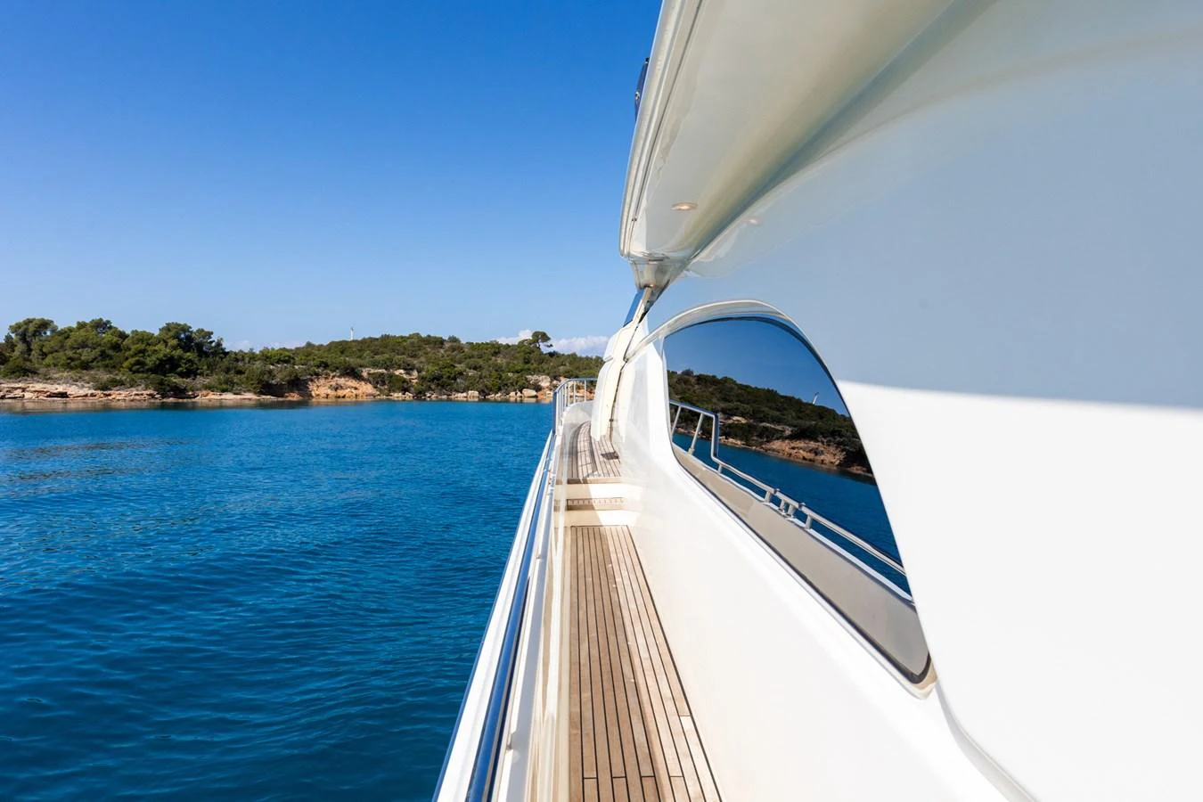 A sleek yacht cruising along a serene coastline with clear blue waters and a bright sky. aboard PUMABAY Yacht for Sale