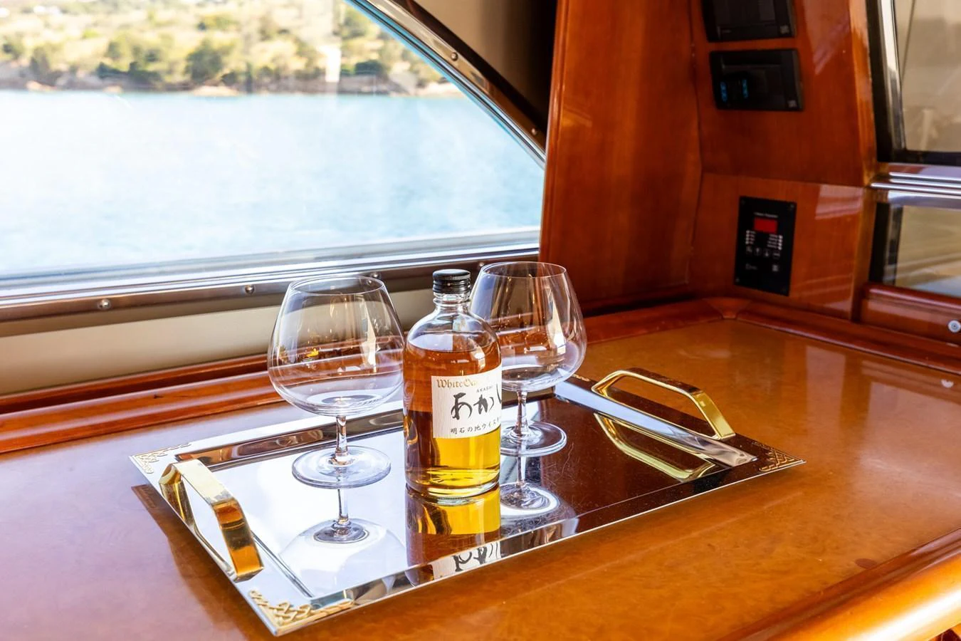 A refined setting with a bottle of whiskey and glasses on a polished wooden surface, framed by a scenic window view. aboard PUMABAY Yacht for Sale
