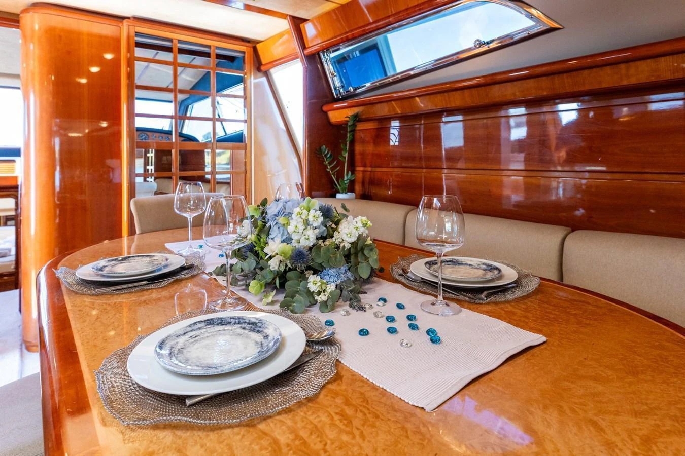 The yacht's dining area features a beautifully set table with elegant tableware and a floral centerpiece, surrounded by rich wooden finishes and ample natural light. aboard PUMABAY Yacht for Sale