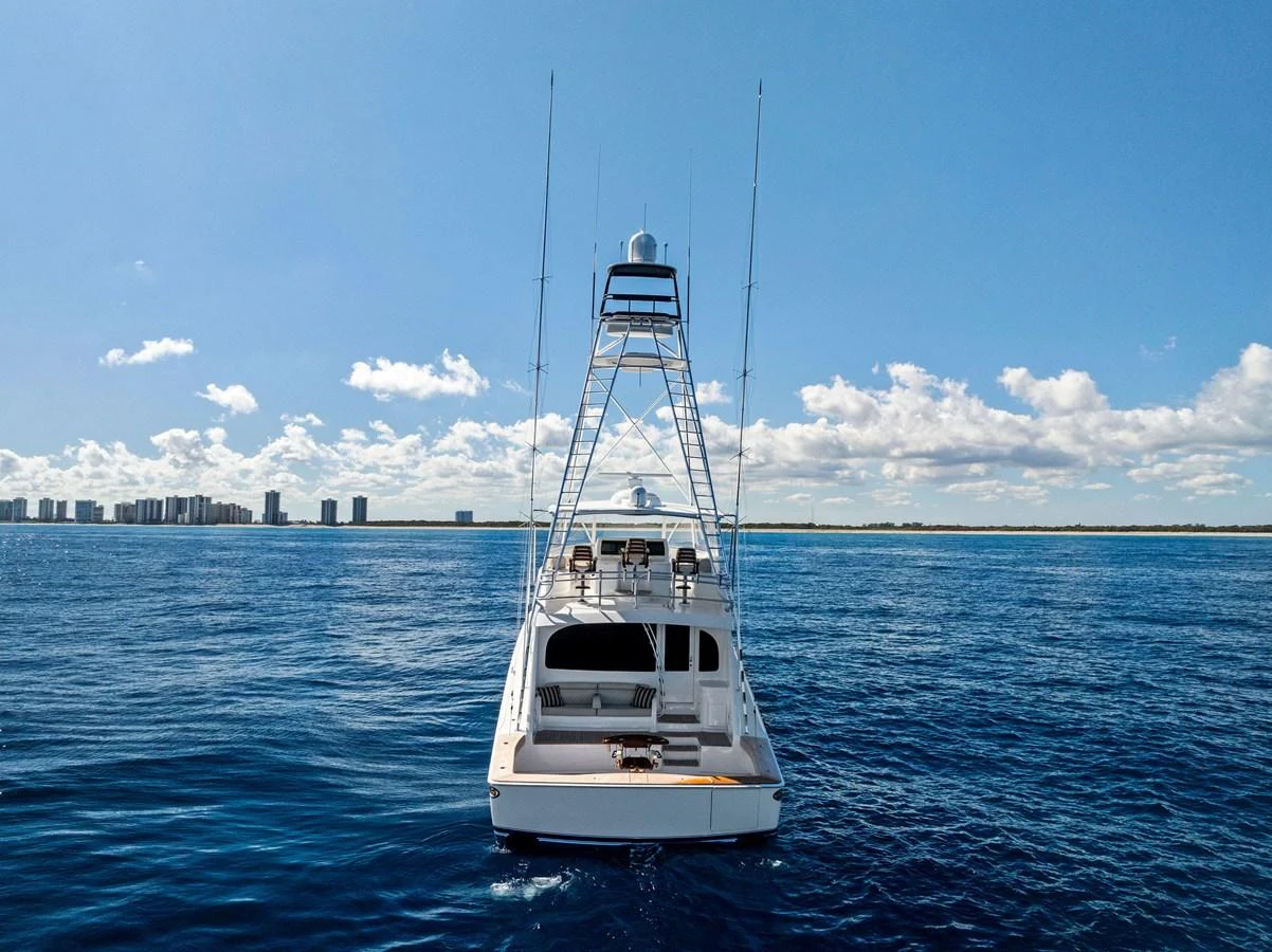 A sleek yacht is seen from the rear, cruising on a calm blue sea with a cityscape in the background. aboard CATCH 23 Yacht for Sale