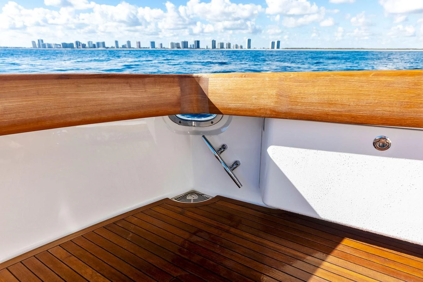 A close-up view of the yacht's teak deck and polished wooden rail with a city skyline in the background. aboard CATCH 23 Yacht for Sale