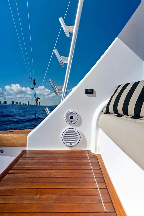 A close-up view of a yacht's deck area with polished wood flooring and a cushioned seating area, set against a backdrop of the ocean and city skyline. aboard CATCH 23 Yacht for Sale