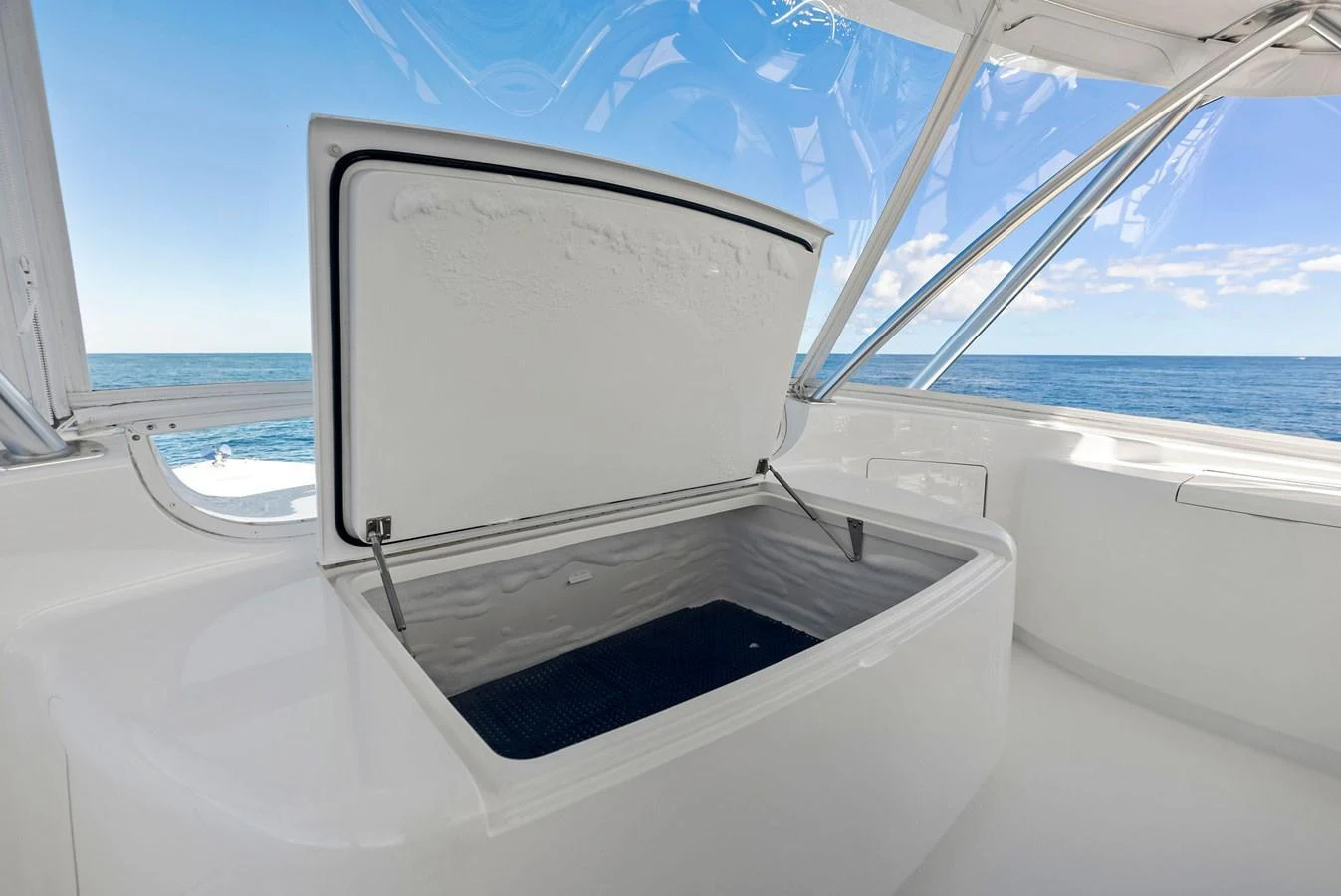 A pristine white storage compartment is open on the deck, revealing a spacious interior against a backdrop of clear blue skies and calm ocean waters. aboard CATCH 23 Yacht for Sale