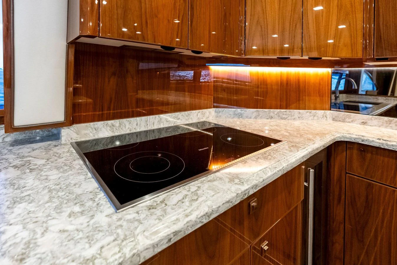 The galley features a sleek induction cooktop set in a luxurious marble countertop with rich wooden cabinetry. aboard CATCH 23 Yacht for Sale