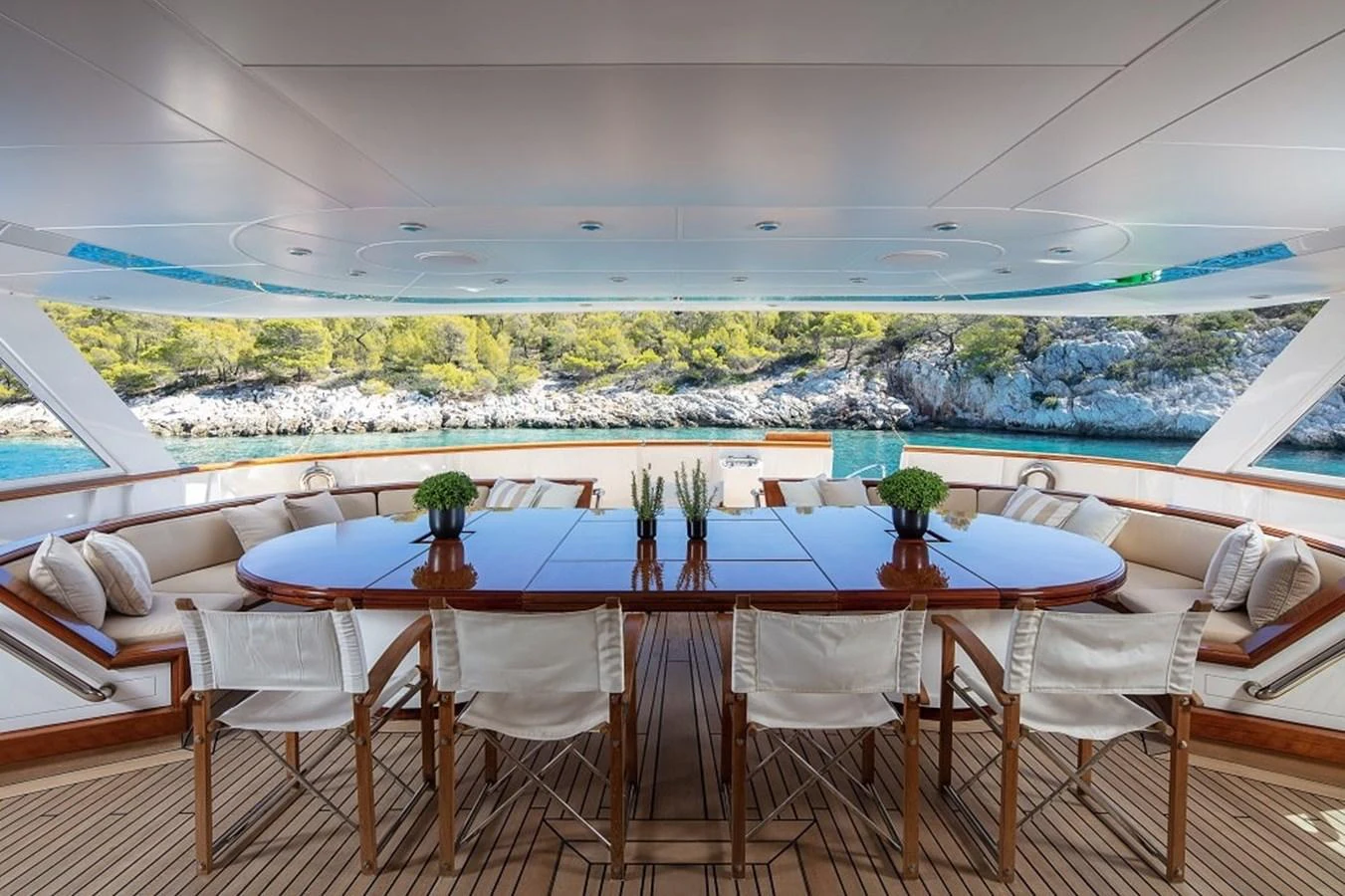 The aft deck features an elegant dining area with a large wooden table and comfortable seating, offering stunning views of the surrounding waters. aboard KASSANDRA Yacht for Sale