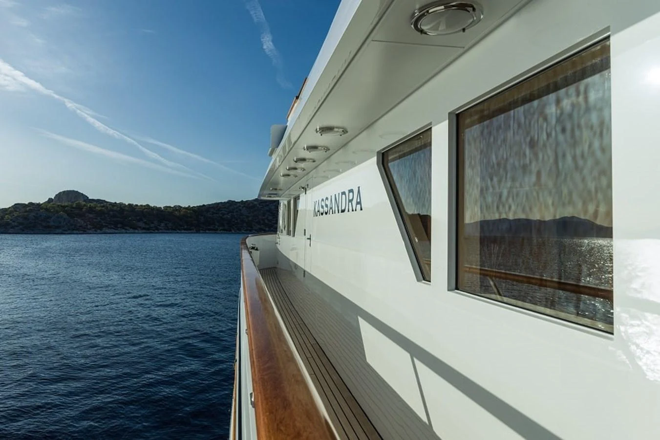 A sleek exterior view of the yacht's side deck with a scenic backdrop of the sea and distant hills. aboard KASSANDRA Yacht for Sale